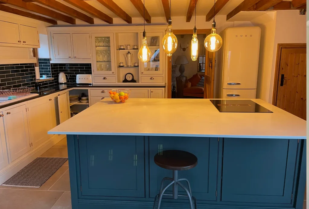 Cream farmhouse kitchen with a teal painted island, induction hob and beamed ceiling
