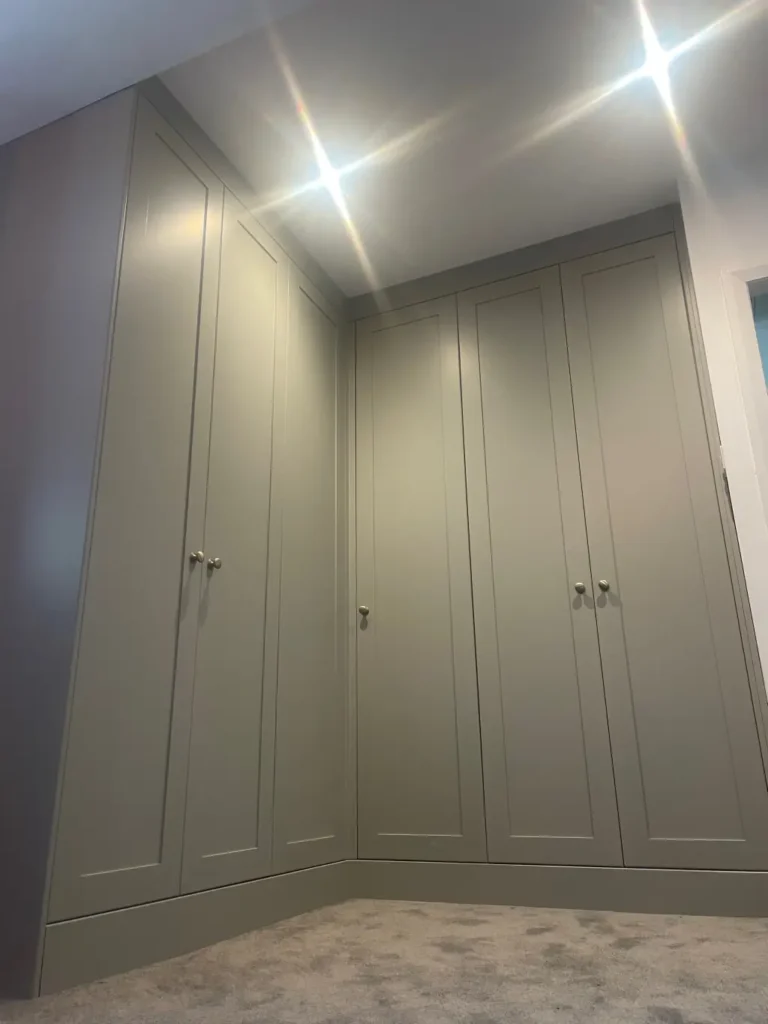 Corner run of floor to ceiling shaker wardrobes painted sage green with brass knobs