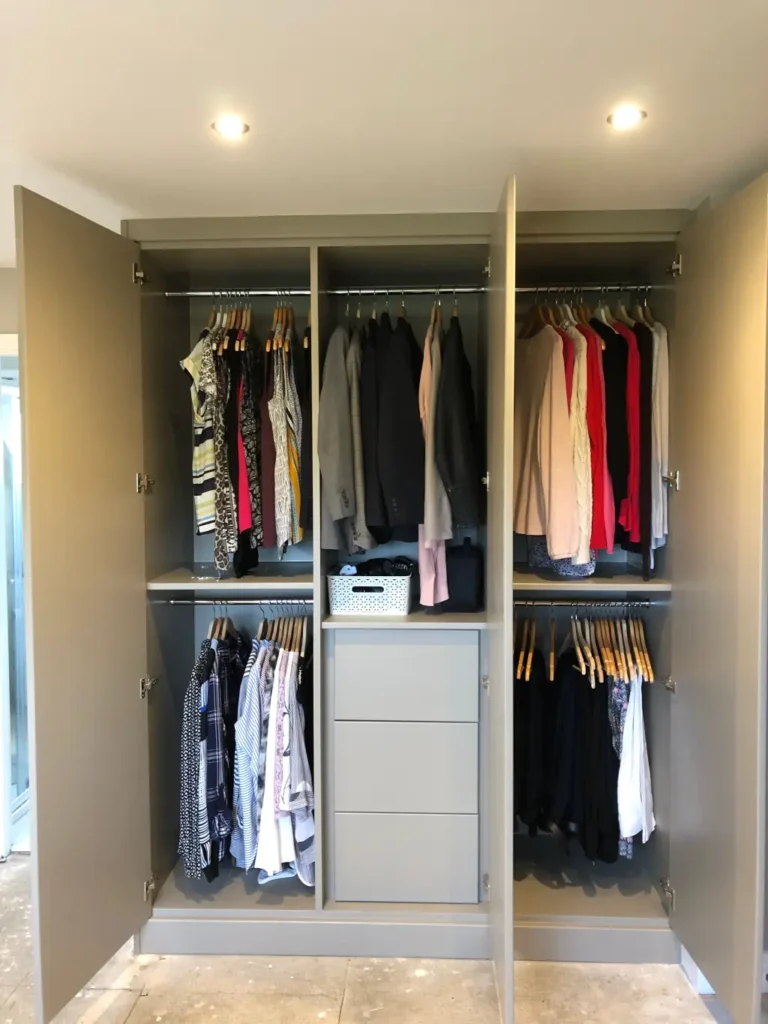 Open grey fitted wardrobe showing hanging rails, clothes and a central drawer stack